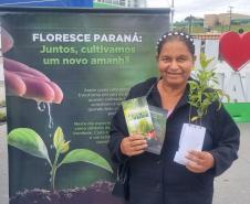 Civil com muda posando para foto a frente do banner "Florescer Paraná"