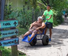 Voluntário transportando idosa em uma cadeira de rodas pelo litoral